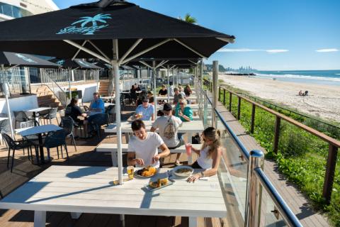 Guests eating on the beachfront deck at Palm Beach Surf Life Saving Club, looking north along the sand