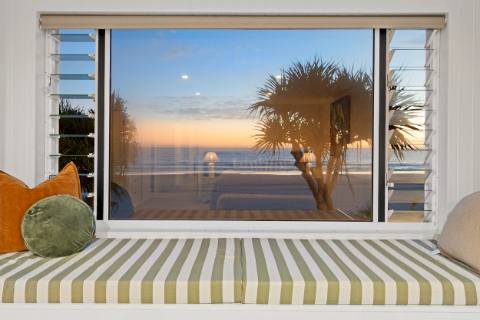 Cushioned window seat looking through pandanus to sunrise over the ocean
